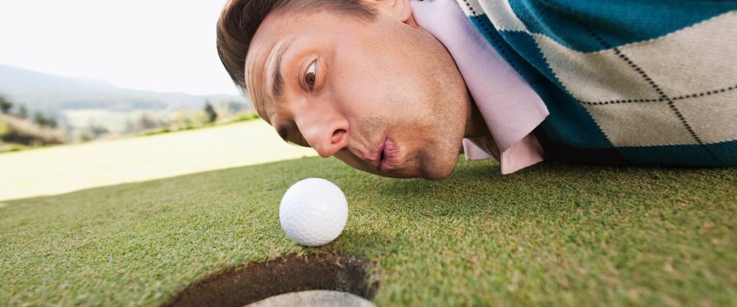 humorous image golfer blowing on golf ball on edge of the cup